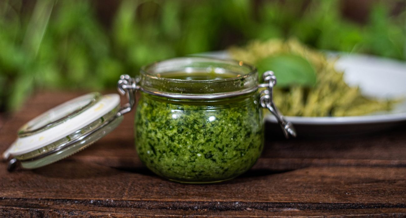 Bote con pesto de Albahaca. Pasta con pesto de fondo.